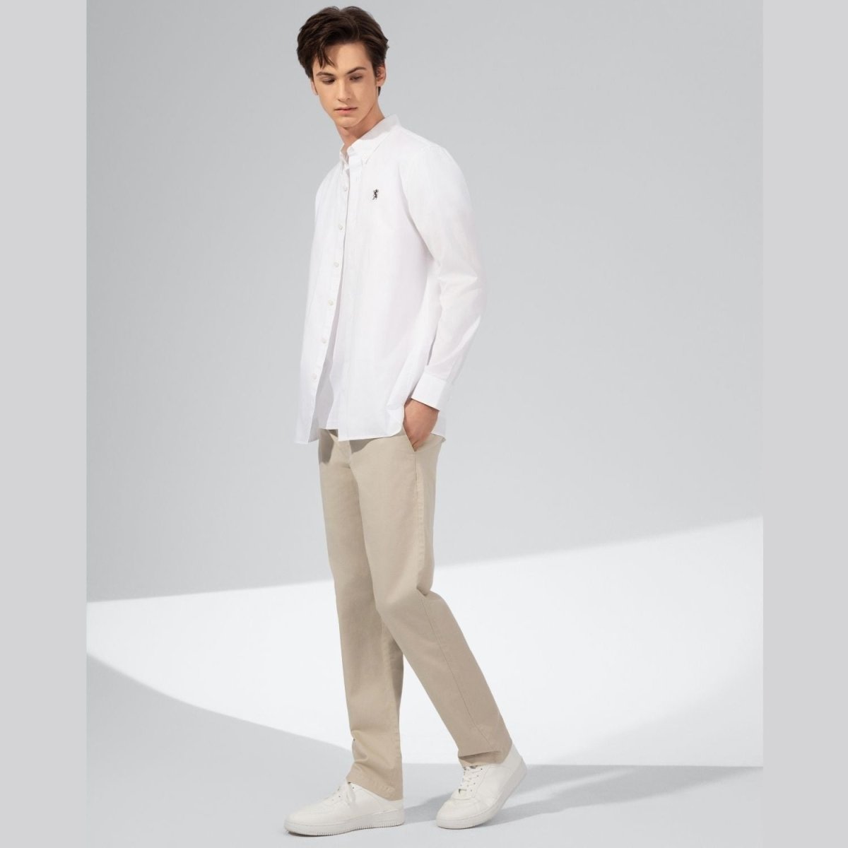 Giordano white oxford shirt with lion embroidery worn by male model with beige pants and white sneakers